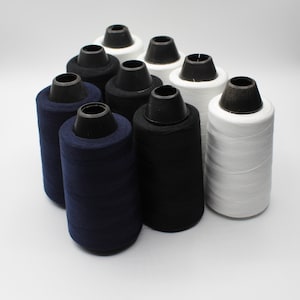 Könnte beinhalten: Eine Sammlung von Garnrollen in Schwarz, Weiß und Marineblau. Die Rollen sind in einem Kreis angeordnet, wobei die weißen Rollen vorne liegen.