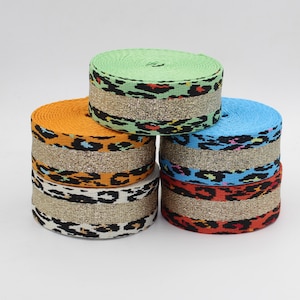 Peut inclure: Cinq bobines de ruban en tissu coloré avec une bande de paillettes dorées. Le ruban a un motif léopard dans différentes couleurs, notamment orange, vert, bleu et rouge.