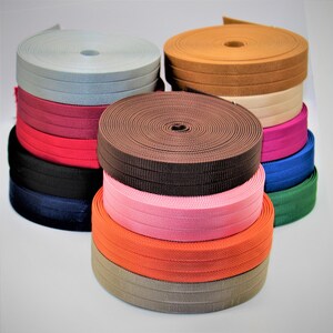 May include: A stack of different colored woven elastic bands. The bands are in various colors, including beige, brown, pink, orange, red, blue, green, and gray.