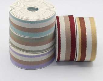 Könnte beinhalten: Vier Rollen gestreiftes Baumwoll-Gurtband. Das Band ist in verschiedenen Farben, darunter beige, braun, rot und blau.