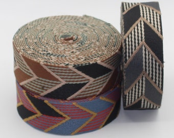 Könnte beinhalten: Drei Rollen dekorativen Bandes mit geometrischen Mustern. Eine Rolle ist eine Spirale aus beigem, braunem und schwarzem Band. Eine weitere Rolle zeigt ein Muster aus schwarzen, roten und blauen Pfeilmustern. Ein drittes Band hat ein Pfeilmuster in Schwarz, Grau und Weiß.
