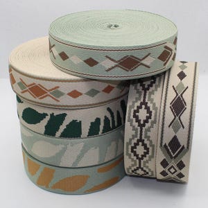 May include: A collection of woven ribbons in various colours and patterns. The ribbons feature geometric and abstract designs in shades of green, brown, and cream. The ribbons are rolled into spools.