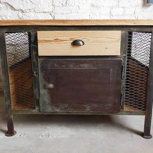 Puede incluir: Gabinete de estilo industrial con tapa y cajón de madera clara. El gabinete presenta un marco de metal con laterales de malla de alambre y una puerta de metal oscuro. El cajón tiene un tirador de metal. Medidas en cm.