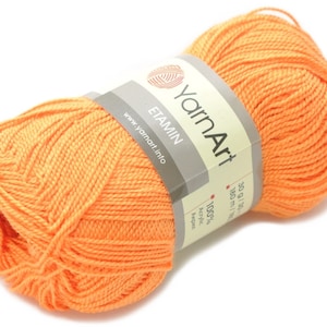 Może przedstawiać: Motka pomarańczowej włóczki z etykietą "YarnArt Etamin" z tekstem "100% akryl" i "30 g / 1.06 oz 180 m / 196 yds" na etykiecie.
