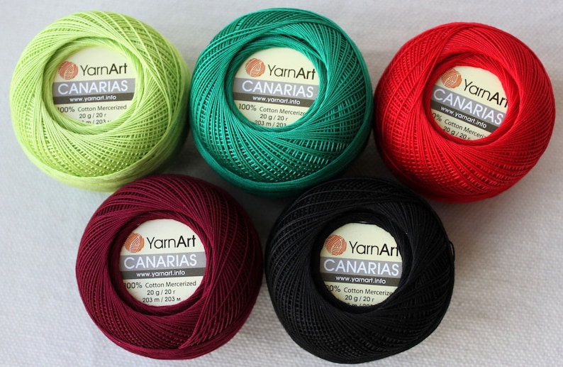 May include: Five balls of yarn in different colors: green, red, burgundy, black, and light green. Each ball has a label that reads "YarnArt CANARIAS" with the company website address and information about the yarn. The yarn is 100% cotton mercerized and comes in 20 gram balls.