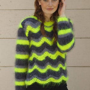 May include: A long-sleeve fuzzy sweater featuring a horizontal chevron pattern in alternating neon yellow, charcoal gray, and light gray stripes. The knit garment has a round neckline and a scalloped hemline with a soft, textured, mohair-like finish.