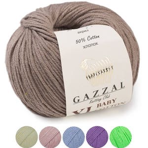 Peut inclure: Une pelote de laine brune étiquetée "Gazal Baby Cotton" avec 50% coton et 50% acrylique. L'étiquette comprend également le texte "Knitting Club". La laine est présentée avec cinq plus petites pelotes de laine de différentes couleurs : vert clair, rose, bleu clair, violet et vert vif.