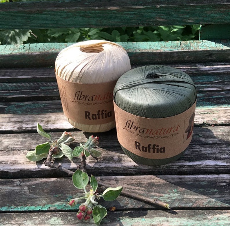 May include: Two spools of natural raffia fiber, one in a natural beige color and one in a dark green color. Both spools have a brown label with the text "fibranatura" and "Raffia".