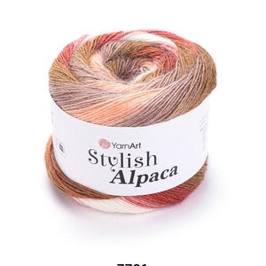 以下が含まれることがあります： 白、桃色、茶色、赤色などの色が混ざったYarnArt Stylish Alpacaの毛糸玉。毛糸は、ブランド名と製品名が記載された白いラベルに巻かれています。製品コード7701が下部に印刷されています。