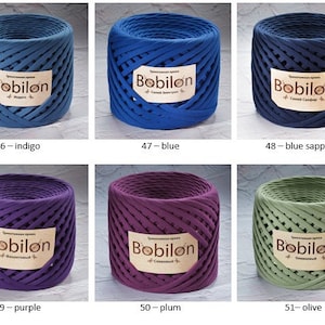 K&ouml;nnte beinhalten: Sechs Spulen aus Baumwollseil in verschiedenen Farben, darunter Indigo, Blau, Saphir, Lila, Pflaume und Oliv. Jede Spule tr&auml;gt ein Etikett mit der Aufschrift "Bobilon".