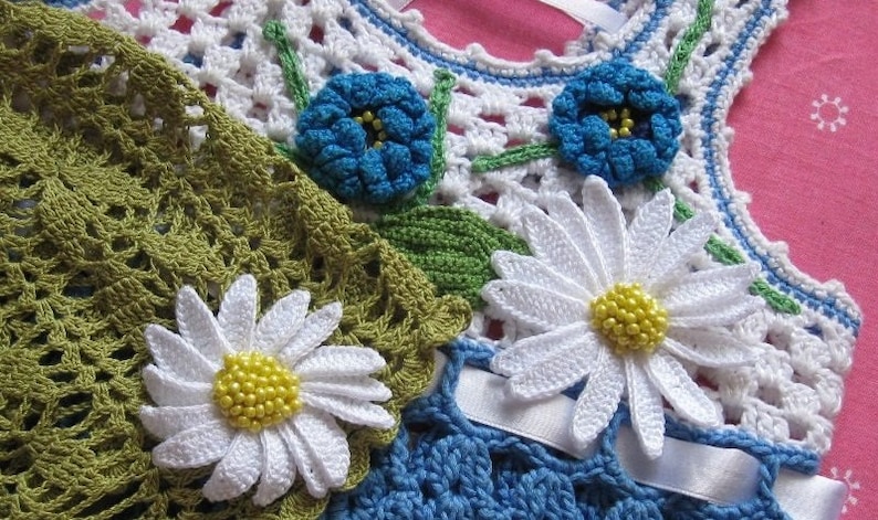May include: A crocheted garment with white, blue, and green flowers. The garment is made with a delicate crochet stitch and features a variety of floral designs.