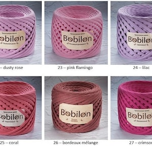 K&ouml;nnte beinhalten: Nahaufnahme von sieben Spulen Baumwollseil in verschiedenen Rosat&ouml;nen, Rot und Lila. Die Spulen sind mit dem Markennamen "Bobilon" und dem Farbnamen beschriftet. Die Farben sind Dusty Rose, Pink Flamingo, Lilac, Coral, Bordeaux M&eacute;lange und Crimson.