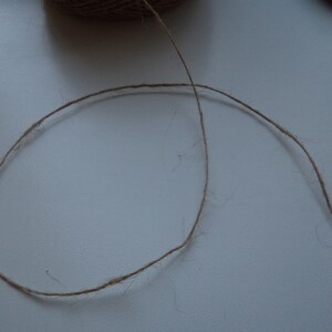 May include: A close-up of a brown twine string on a white surface.