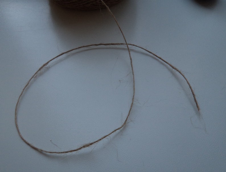 May include: A close-up of a brown twine string on a white surface.