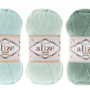 Pode incluir: Três novelos de fio Alize Cotton Gold hobby dispostos lado a lado. Cada novelo apresenta um rótulo de papel com o texto cotton club alize Cotton Gold hobby. As cores do fio variam de um verde menta claro a um verde sálvia médio.