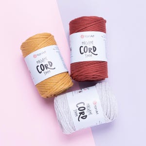 May include: Three spools of YarnArt macrame cord, each 3mm in diameter. The spools are colored mustard yellow, terracotta red, and light gray. Each spool features a white paper label with the brand name and product details printed in black text.