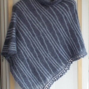 May include: A blue knitted poncho featuring a high cowl neckline and a diagonal striped pattern in lighter blue tones. The garment has a textured, fuzzy appearance and is finished with a delicate, openwork crocheted lace trim along the bottom edge.