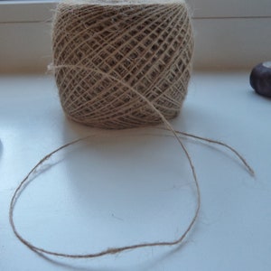 May include: A ball of natural twine with a long piece of twine extending from it. The twine is on a white surface.