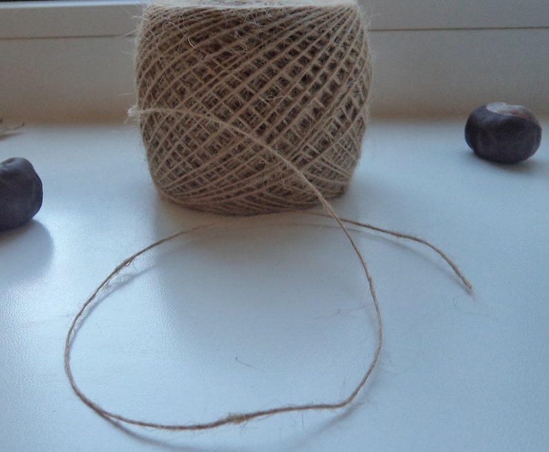 May include: A ball of natural twine with a long piece of twine extending from it. The twine is on a white surface.