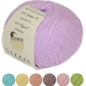 以下が含まれることがあります： ライトパープルの糸の玉で、ラベルには「メリノウール 20% カシミヤ Pa カシミヤ Pa 40% ポリアクリル ポリアクリル GAZZAL ニッティングクラブ」と書いてあります。