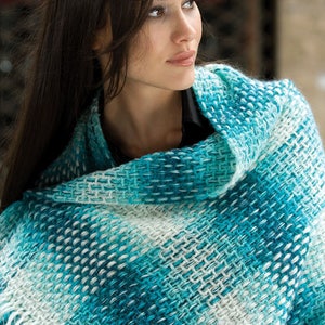 Puede incluir: Una mujer lleva una estola de color azul verdoso y blanco con flecos. La estola est&aacute; hecha de un tejido suave y tejido.