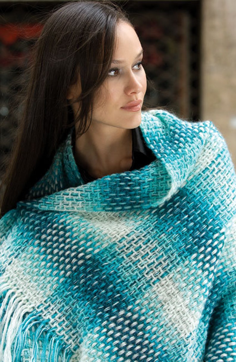 Puede incluir: Una mujer lleva una estola de color azul verdoso y blanco con flecos. La estola est&aacute; hecha de un tejido suave y tejido.