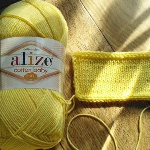 May include: A skein of yellow cotton baby yarn with the label "alize cotton baby soft" and a small knitted swatch of the yarn.