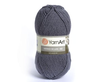 May include: A ball of dark gray YarnArt Merino de Luxe /50 yarn. The yarn is tightly wound and has a textured appearance. A label wraps around the center of the ball, displaying the brand name and product details.