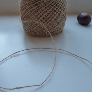 May include: A ball of natural twine with a long strand of twine extending from it. The twine is on a white surface.