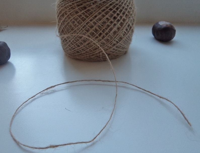May include: A ball of natural twine with a long strand of twine extending from it. The twine is on a white surface.