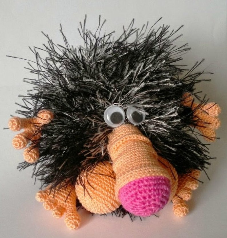 May include: A black and white fuzzy crocheted toy with a long orange nose and pink nose tip. The toy has large black eyes and orange crocheted arms and legs.
