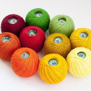 Puede incluir: Una colecci&oacute;n de diez ovillos de lana en varios tonos de naranja, amarillo, verde y rojo. Los ovillos de lana est&aacute;n dispuestos en c&iacute;rculo.