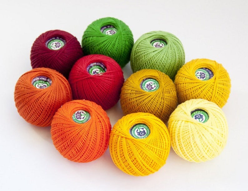 Puede incluir: Una colecci&oacute;n de diez ovillos de lana en varios tonos de naranja, amarillo, verde y rojo. Los ovillos de lana est&aacute;n dispuestos en c&iacute;rculo.