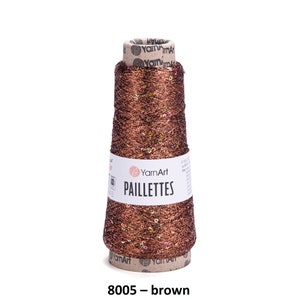 May include: A spool of brown yarn with gold glitter and sequins. The yarn is labeled "YarnArt Paillettes 8005 - brown".