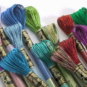 May include: Assortment of DMC metallic embroidery floss spools in various colors, including silver, blue, green, red, purple, and iridescent. Each spool is labeled with the DMC brand name and "Metallic" in French.