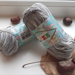 May include: Two skeins of gray and white yarn with a blue and white label that says "COLOR LOT 50886 - 660600" and "Prizze romantika" in a floral design.