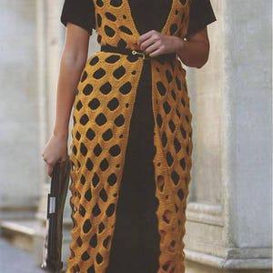 May include: A woman wearing a long, yellow crochet vest with a black top and black shoes. The vest has a geometric pattern and is open in the front. The woman is wearing sunglasses and a belt.