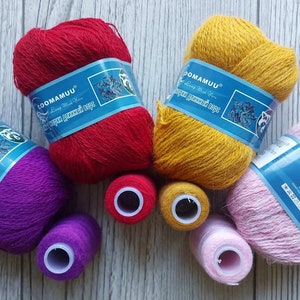 Könnte beinhalten: Fünf Knäuel Garn in verschiedenen Farben: Lila, Rot, Gelb, Rosa und ein kleineres Knäuel Rot. Das Garn ist mit "COOMAMUU" und "COOG" gekennzeichnet.