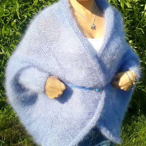 May include: A light blue, fuzzy, open-front knit cardigan with long sleeves and a wide shawl collar. The garment is cinched at the waist with a thin, matching light blue belt. The knit texture appears soft and slightly brushed, creating a halo effect.