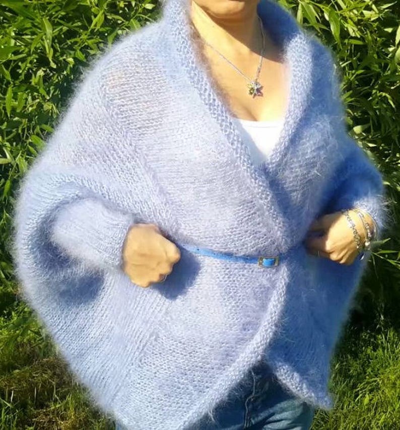 May include: A light blue, fuzzy, open-front knit cardigan with long sleeves and a wide shawl collar. The garment is cinched at the waist with a thin, matching light blue belt. The knit texture appears soft and slightly brushed, creating a halo effect.