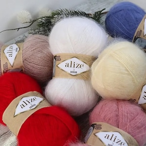 Op de afbeelding: Assortiment van kleurrijke garenklossen in verschillende tinten roze, rood, wit, beige, geel en blauw. Elke klos heeft een label met de merknaam "alize" en de tekst "3 season".