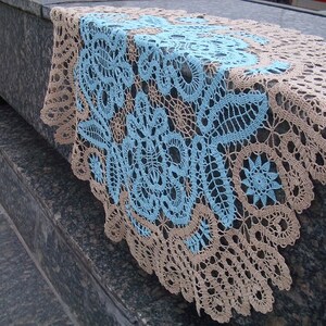 May include: A delicate crocheted tablecloth with a blue and beige floral pattern. The tablecloth is made of fine thread and has a delicate lace trim.
