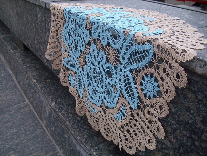 May include: A delicate crocheted tablecloth with a blue and beige floral pattern. The tablecloth is made of fine thread and has a delicate lace trim.