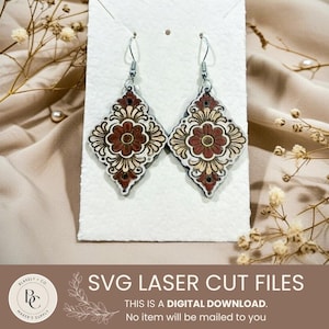 May include: Pair of ornate, laser-cut earrings with a floral design. The earrings feature a diamond shape with a central flower in shades of brown, cream, and black. The text "SVG LASER CUT FILES" and other text is visible at the bottom.