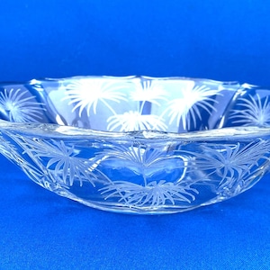 May include: A clear glass bowl featuring a delicate etched palm leaf pattern around the exterior. The bowl has a scalloped rim and two small, decorative handles on opposite sides, providing a functional and detailed design for serving.