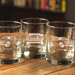 Puede incluir: Cuatro vasos transparentes de vidrio con un contorno blanco de un coche Chevrolet Chevelle de 1967 grabado en cada vaso. Los vasos est&aacute;n sobre una superficie de madera.