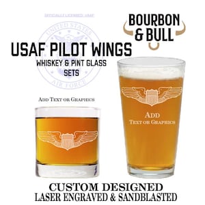 May include: Two glass sets, one whiskey glass and one pint glass, with a laser engraved design of the United States Air Force pilot wings. The text "USAF PILOT WINGS" is above the glasses, and the text "BOURBON & BULL" is in the upper right corner. The text "CUSTOM DESIGNED LASER ENGRAVED & SANDBLASTED" is below the glasses.