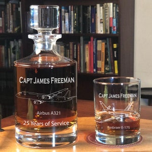 May include: A clear glass decanter and a matching tumbler filled with amber liquid. The decanter is etched with Capt James Freeman, an Airbus A321, and 25 Years of Service. The tumbler is etched with Capt James Freeman and an Embraer E-175.
