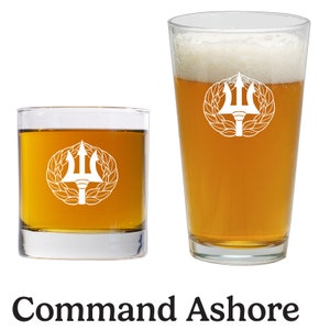 May include: Two glasses of beer, one a pint glass and one a smaller glass, both with a white design of a trident and a wreath. The text "Command Ashore" is below the glasses.
