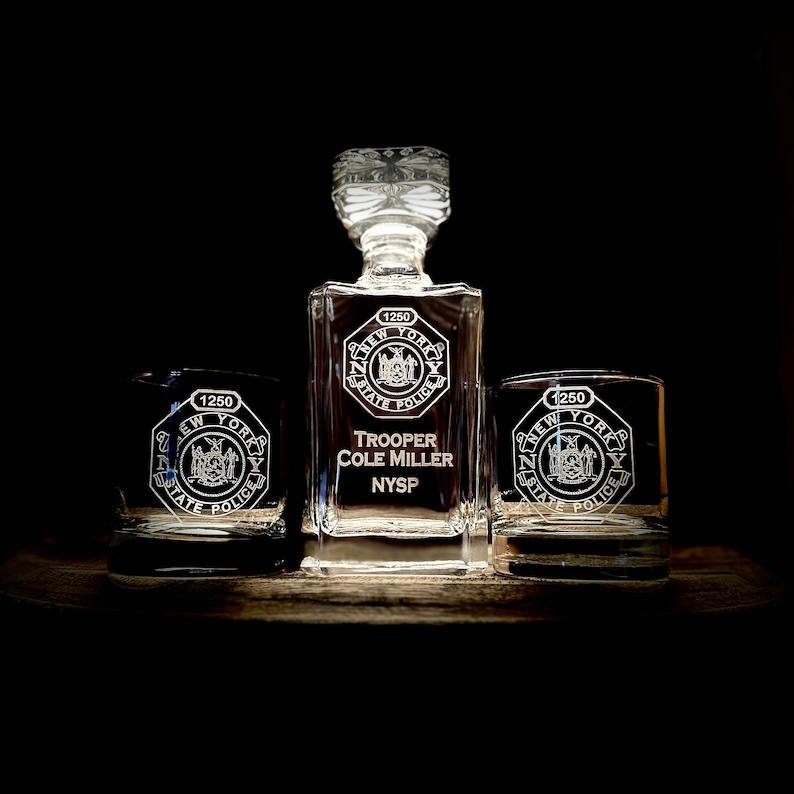 May include: A crystal decanter and two matching glasses engraved with a New York State Police badge and the text "Trooper Cole Miller NYSP".